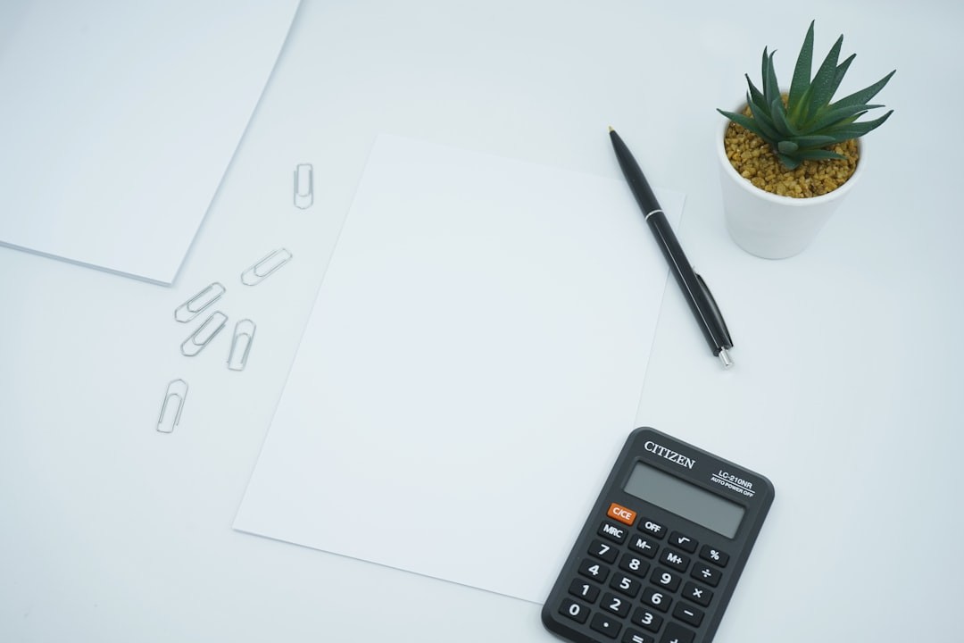 A financial and money themed photo featuring a blank paper on a desk next to a pen and calculator. Crunch the numbers!